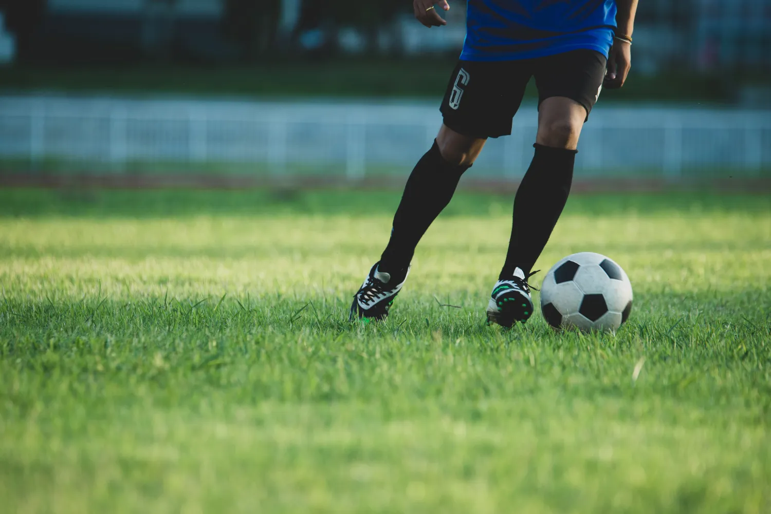 A footballer in a blue shirt running with the ball on a sunlit pitch