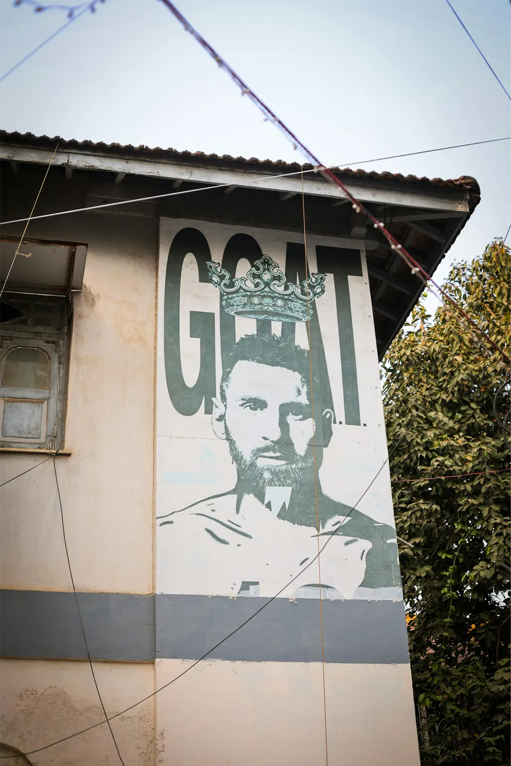 A large mural of Lionel Messi wearing a painted crown above the word GOAT on the side of a building